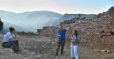 Discussion à l'aube, en juillet 2021, avant le début d'une journée de fouille. Derrière les archéologues, une section des remparts tardifs de Delphes et le paysage matinal des hautes vallées de Phocide. Ministère grec de la culture/Ecole française d'Athènes/Mission fortifications de Delphes/K. Robert


