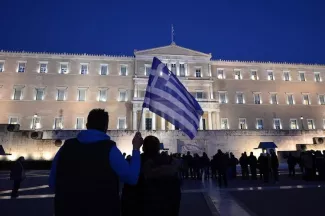 Athènes garde la tête hors de l'eau, mais sous haute surveillance Un homme tient un drapeau grec devant le parlement à Athènes le 20 février 2015 (Photo Louisa Gouliamaki. AFP)