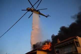 Un hélicoptère largue de l'eau sur une maison en feu pendant un incendie à Kryoneri, près d'Athènes, le 26 juillet 2025.