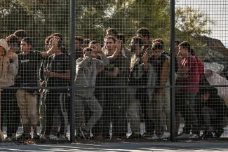 Des migrants sont rassemblés par les gardes-côtes grecs, derrière une clôture, après avoir débarqué d'un cargo dans le port de Lavrio, à Athènes, le 10 juillet 2025. ARIS MESSINIS / AFP