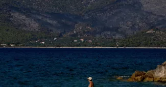 Des baigneurs à Alepochori, en Grèce, face au village côtier de Psatha, ravagé par un feu de forêt, le 4 août 2026.