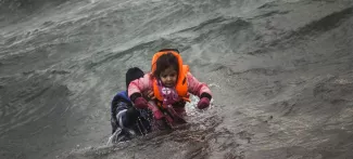 Grèce: l'île de Lesbos est dépassée par le flux de migrants Après être tombés de leur canot pneumatique au moment de débarquer, un homme porte une petite fille pour l'aider à atteindre le rivage de l'île de Lesbos, dimanche 3 janvier. Crédits photo : Santi Palacios/AP