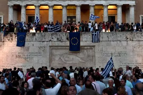 Des manifestants pro-Europe agitent des drapeaux grecs et européens devant le parlement à Athènes. Ils espèrent ainsi que Tsipras dise oui à la proposition des créanciers. Sur un mur de la ville, des tagueurs ont enterré l'euro. © AFP.


