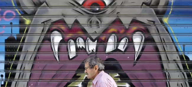 Un homme passe devant la devanture fermée d'un magasin dans le centre-ville d'Athènes. Crédits photo : CHRISTIAN HARTMANN/REUTERS


