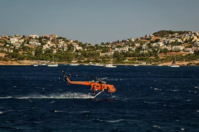 Un hélicoptère de lutte contre les incendies Erickson se remplit d'eau dans la mer lors d'un incendie de forêt à Palaia Fokaia, à environ 43 km au sud d'Athènes, le 9 août 2025.  -  Aris MESSINIS - Palaia Fokaia (AFP)