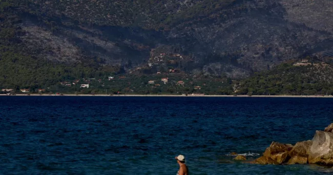 Des baigneurs à Alepochori, en Grèce, face au village côtier de Psatha, ravagé par un feu de forêt, le 4 août 2026.