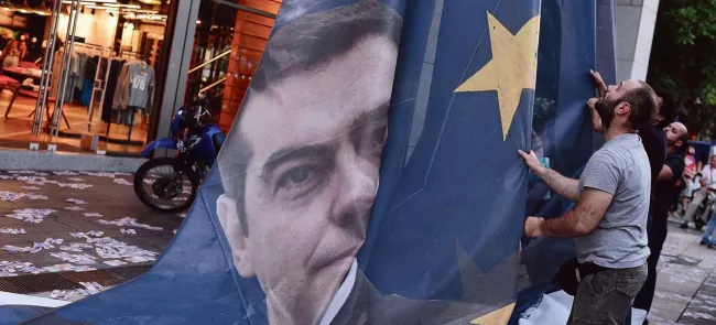 Des manifestants décrochent un drapeau à l'effigie d'Alexis Tsipras sur fond d'emblème européen, à Athènes, le 11 juin. Crédits photo : LOUISA GOULIAMAKI/AFP


