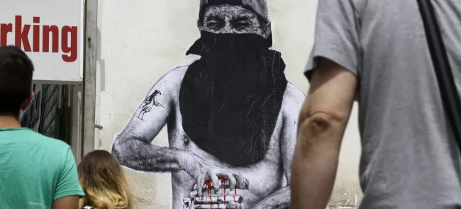 De jeune grecs passent devant une peinture de rue représentant un manifestant en train de compresser jusqu'au sang le symbole de l'euro, lundi 22 juin à Athènes. Crédits photo : Thanassis Stavrakis/AP


