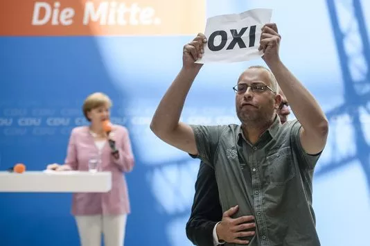 Un homme brandit un papier qui clame non en grec, la veille du référendum. Angela Merkel donnait un discours dans le cadre d'un meeting de la CDU, à Berlin le 4 juillet.


