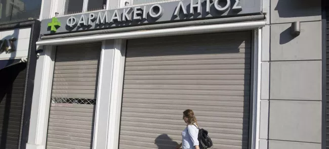 Dans les rues d'Athènes, une femme passe devant une pharmacie fermée pour cause de grève. Crédits photo : Petros Giannakouris/AP


