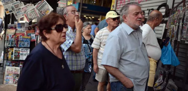Des Grecs lisent les titres des journaux, au lendemain de l'annonce de la démission d'Alexis Tsipras. (LOUISA GOULIAMAKI / AFP)


