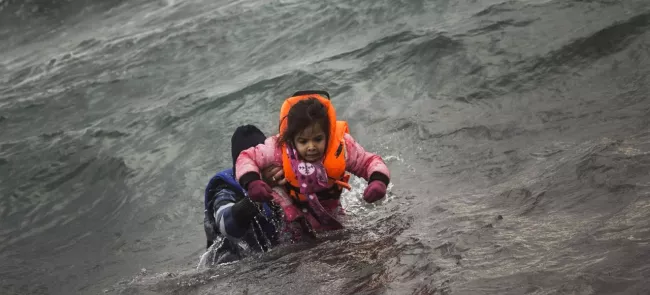 Après être tombés de leur canot pneumatique au moment de débarquer, un homme porte une petite fille pour l'aider à atteindre le rivage de l'île de Lesbos, dimanche 3 janvier. Crédits photo : Santi Palacios/AP


