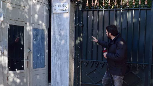 Un journaliste montre l'endroit où les éclats de la grenade ont frappé l'entrée du bâtiment.


