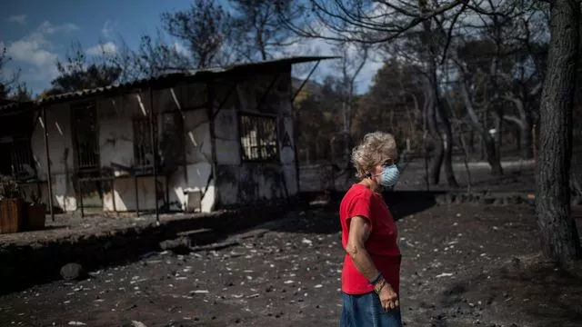 Une femme tente de se protéger des émanations de fumée devant sa maison du village de Neos Voutzas le 26 juillet 2018


